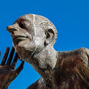 Bronzefigur hält Hand an Ohr
