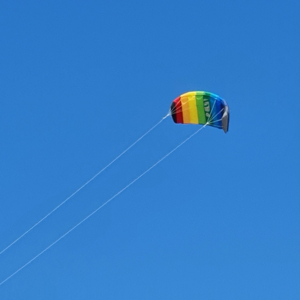 Kiteschirm in Regenbogenfarben vor blauem Himmel
